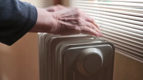 Hands Resting On A Small Radiator By Window Blinds In A Cozy Home Heating Scene Stock Footage 327957277