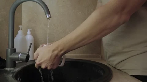 Hands rinsing ceramic mug under running kitchen faucet Stock Footage 340016689