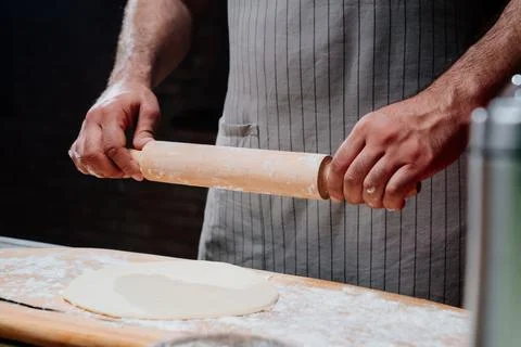 Hands roll the dough into a thin layer. Cooking pizza, noodles or pitta at home Stock Photos