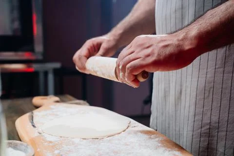 Hands roll the dough into a thin layer. Cooking pizza, noodles or pitta at home Stock Photos