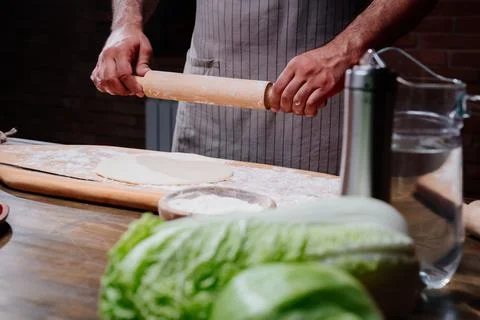 Hands roll the dough into a thin layer. Cooking pizza, noodles or pitta at home Stock Photos