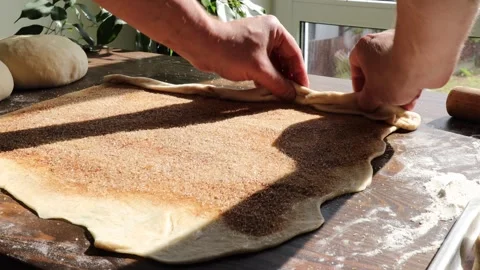Hands roll up flattened dough layered with cinnamon sugar into a log for Stock Footage 310337535
