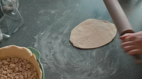 Hands roll out dough on a clean kitchen countertop, shaping it into a round pie Stock Footage 339094541