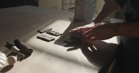 Hands roll texture tools over a clay slab, creating detailed patterns. The Stock Footage 301455431