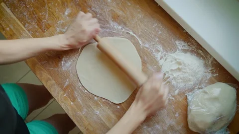Hands rolling dough on wooden surface with rolling pin and flour nearby. Fingers Stock Footage 303094082