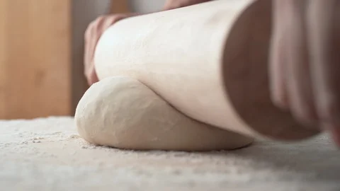 Hands rolling a dough on wooden table. Slow Motion. Stock Footage 128964869