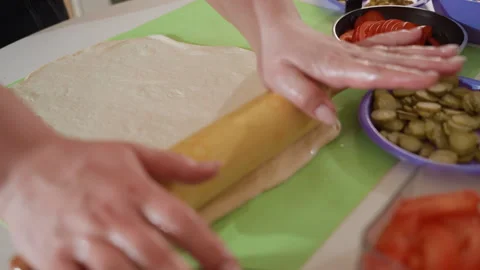 Hands rolling patterned rolling pin over dough on green silicone mat for pizza Stock Footage 345657629