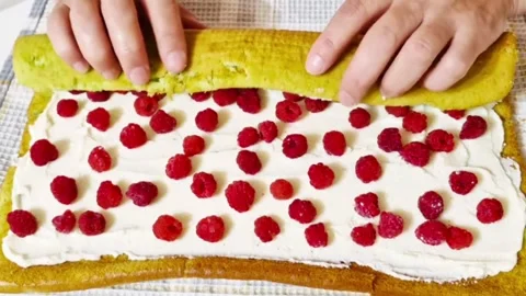 Hands rolling a pistachio sponge cake with cream and fresh raspberries filling Stock Footage 327259043