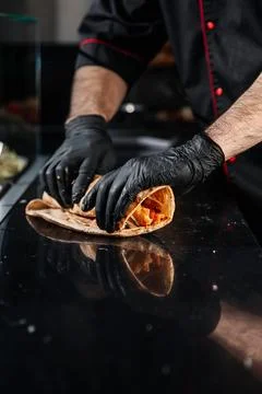 Hands rolling a shawarma wrap with fresh ingredients inside. Stock Photos