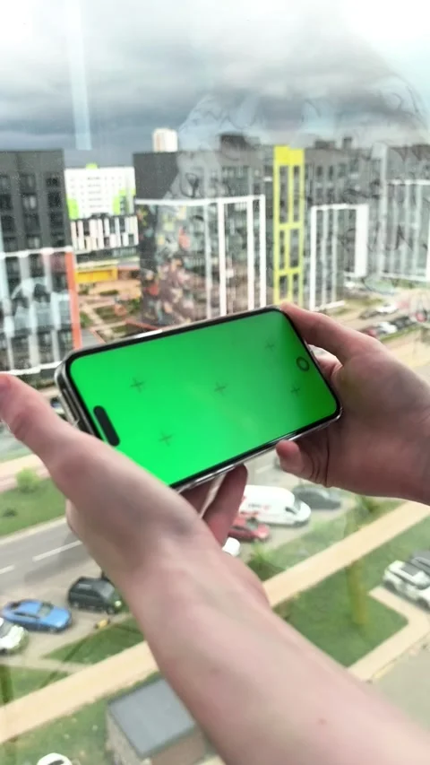 Hands rotate smartphone with green screen near a city window. Device shifts.. Stock Footage 336276017
