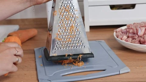 Hands rub fresh carrots on a grater in the kitchen Stock Footage 318463548