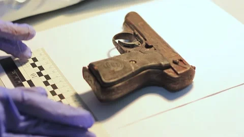 Hands in rubber gloves are examining a weapon, namely a pistol using a forensic Stock Footage 220799344