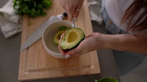 Hands Scooping out fresh avocado into bowl, cooking in kitchen 库存影片 220754768