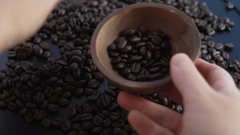 Hands scooping roasted coffee beans into a wooden bowl, 4K close up lifestyle Video stock 329594453