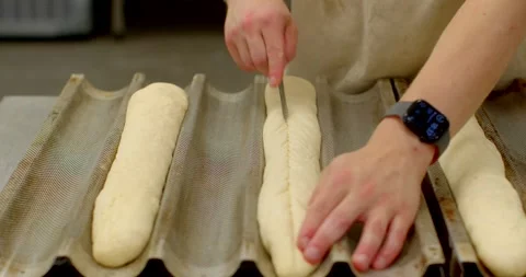 Hands scoring baguette dough in corrugated proofing tray with baker at workbench Stock Footage 344596935