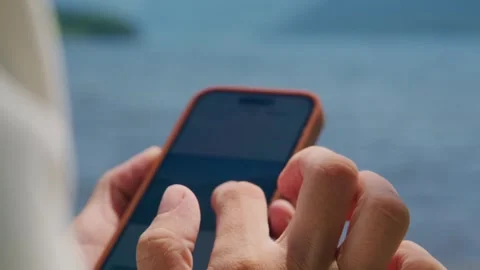 Hands scroll phone near ocean, calm and engaged Stock Footage 345710127