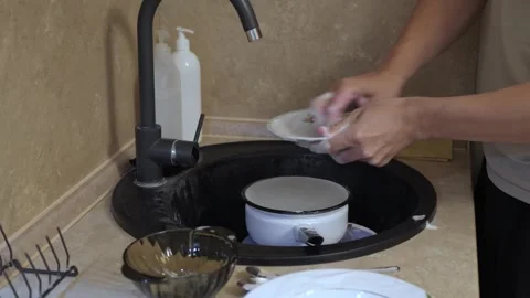 Hands scrubbing a plate in sink under running faucet with sponge Stock Footage 340015914