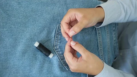 Hands of a seamstress threading a needle on the background of jeans Stock Footage 223225025