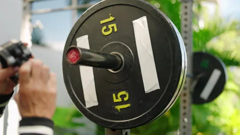 Hands secure jaw lock on barbell for safe lifting at sunny outdoor gym. Fit Stock Footage 280288279