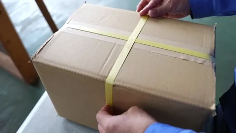 Hands securing cardboard shipping box strapped with yellow plastic banding Stock Footage 340277442