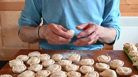 Hands of senior man cooking and molding small homemade uncooked dumplings Stock Footage 142679374