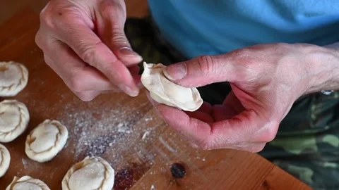 Hands of senior man cooking and molding small homemade uncooked dumplings Stock Footage 142679376