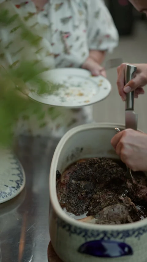 Hands serving roasted meat from ceramic pot onto plate during home dinner Stock Footage 345268778