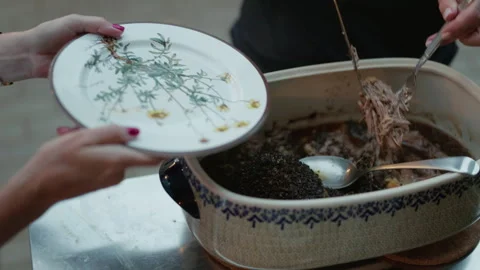 Hands serving roasted meat from ceramic casserole dish onto floral dinner plate Stock Footage 345271641