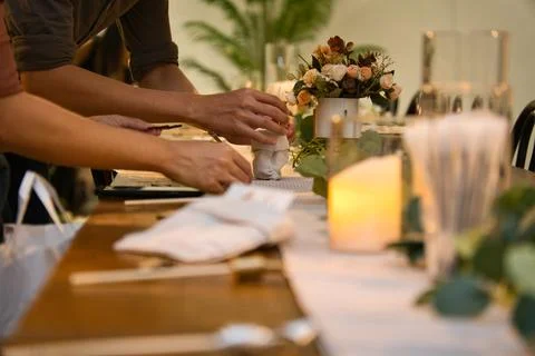 Hands setting up dining table with flowers and candles for an event. Stock Photos
