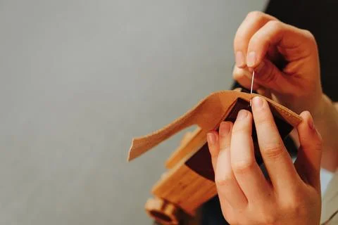 Hands sew a leather edge with needle and thread while secured in a wooden s.. Stock Photos
