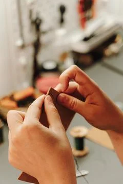 Hands sew a leather edge with needle and thread while secured in a wooden Stock Photos