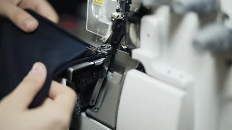 Hands sewing fabric on industrial overlock machine in textile workshop Stock Footage 320256822