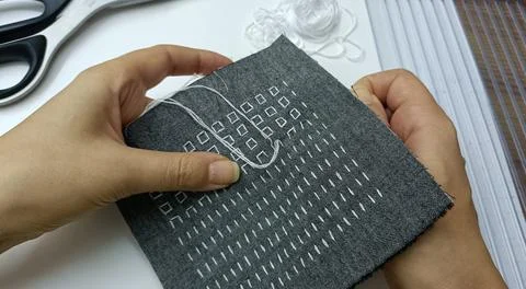 Hands Sewing Geometric Pattern on Dark Fabric Foto stock