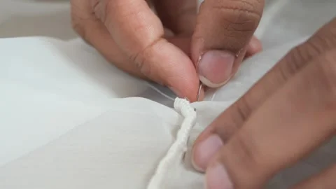 Hands sewing thin white fabric with needle and thread in close up motion. Stock Footage 333258864