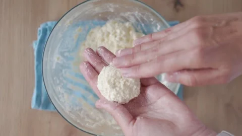 Hands shape cottage cheese dough ball over bowl with mixture on table Stock Footage 337139128