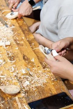 Hands shape wood on rustic table. Shavings scatter across worn surface. Foto stock
