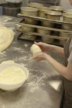 Hands shaping dough in bakery kitchen beside stacked tins and flour dusting Stock Photos