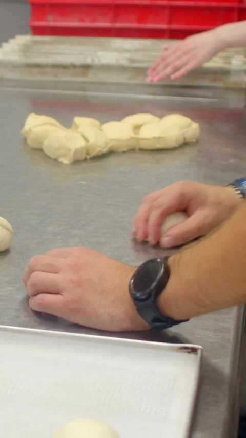 Hands shaping dough balls on stainless steel counter in bakery pastry prep work 库存影片 344576454