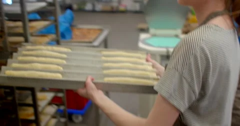 Hands shaping dough logs on stainless bakery counter with tray in foreground Stock Footage 344597987