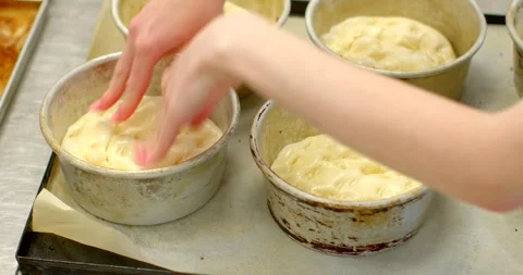 Hands shaping raw dough inside round metal baking molds on commercial, with Видео 344582627
