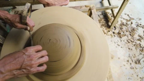 Hands shaping spinning clay with a tool on a pottery wheel, top view 스톡 동영상 348259071