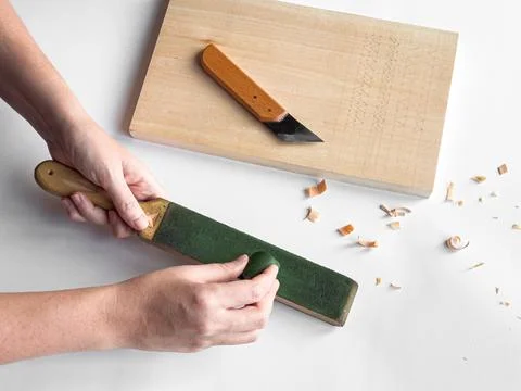 Hands sharpening tool with strop next to cutting board and carving knife Stock Photos