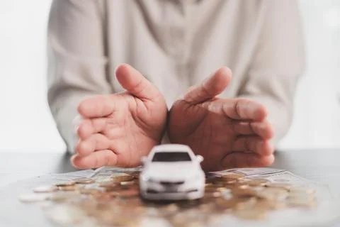 Hands sheltering a white model car over coins and banknotes symbolize vehic.. Stock Photos