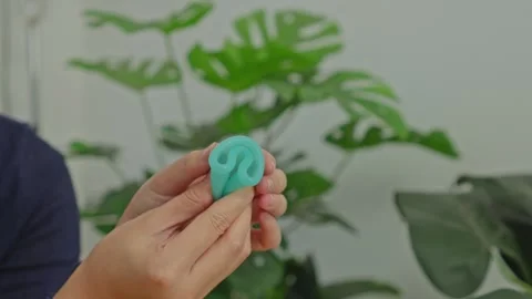 Hands showing C-fold method on green eco-friendly menstrual cup with houseplant Stock Footage 340578836