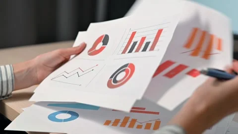 Hands shuffle through various printed charts and graphs while writing notes with Video stock 339005886