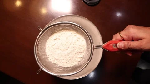 Hands Sifting white All purpose flour through a metal sieve into a bowl for.. Stock Footage 334728886