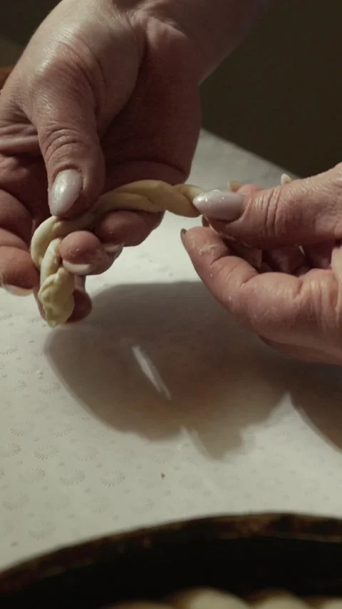 Hands of a skilled baker shaping dough into intricate braided patterns on a Stock Footage 339298814