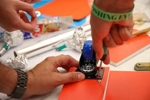 Hands skillfully attaching a blue caster wheel to a vibrant red board using a Stock Photos