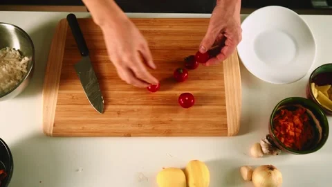 Hands skillfully chop tomatoes and prep various vegetables on a wooden cutting Video stock 316635733