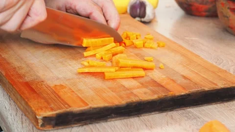 Hands skillfully chop vibrant carrots on a wooden cutting board. The warm Stock Footage 316474435